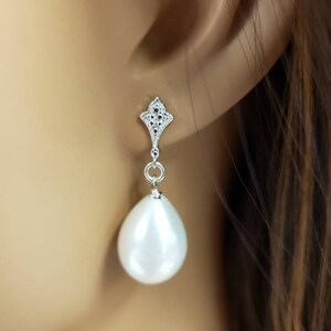 May include: A pair of silver dangle earrings with a white pearl drop. The earrings feature a delicate, intricate design with small clear stones.