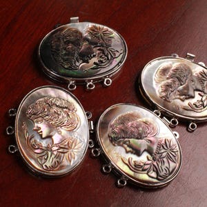 May include: Four oval-shaped, iridescent mother-of-pearl pendants with silver-toned metal clasps. Each pendant features a carved design of a woman's face with intricate details.
