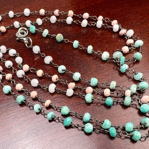 Puede incluir: Un collar de múltiples hilos con una cadena plateada y cuentas en tonos rosa, blanco y turquesa.