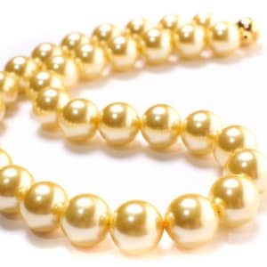 Puede incluir: Una hebra de perlas doradas, enhebradas en un estilo de collar clásico. Las perlas son lisas y lustrosas, con un color crema suave.