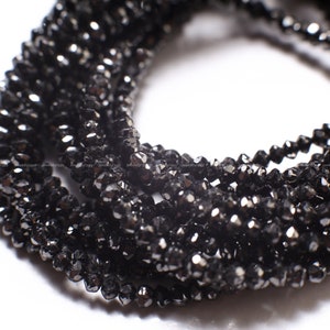 Puede incluir: Primer plano de hebras de cuentas negras facetadas. Las cuentas son pequeñas, con múltiples facetas que capturan la luz, creando un efecto brillante. Las cuentas están ensartadas, formando múltiples hebras. El fondo es blanco.