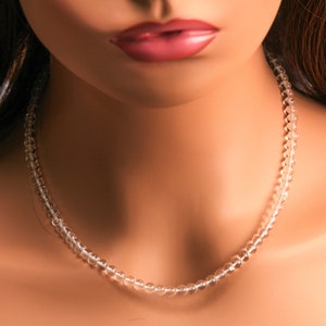 May include: A clear crystal beaded necklace on a model's neck. The necklace is made of small, round beads that are strung together on a thin wire.