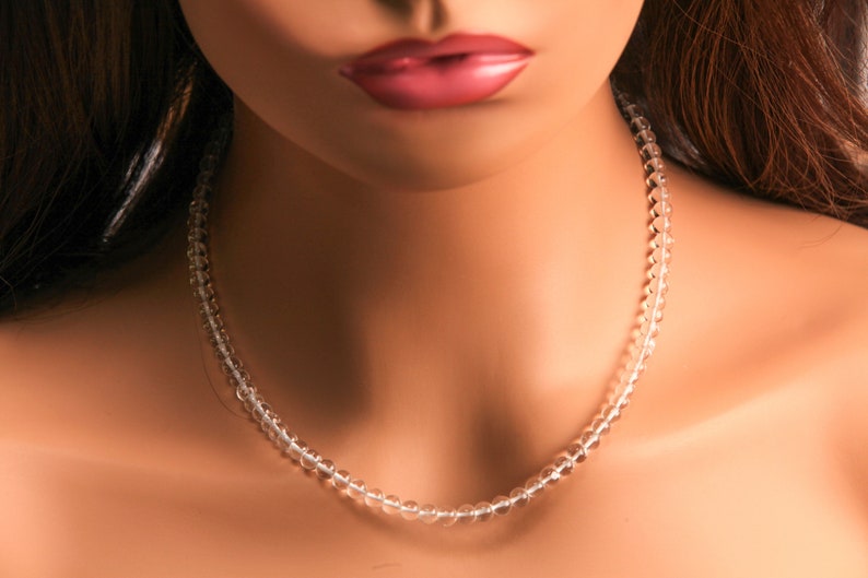 May include: A clear crystal beaded necklace on a model's neck. The necklace is made of small, round beads that are strung together on a thin wire.