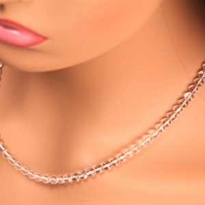 May include: A clear crystal beaded necklace on a mannequin. The necklace is made of small, round beads that are strung together on a thin cord.