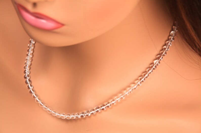 May include: A clear crystal beaded necklace on a mannequin. The necklace is made of small, round beads that are strung together on a thin cord.