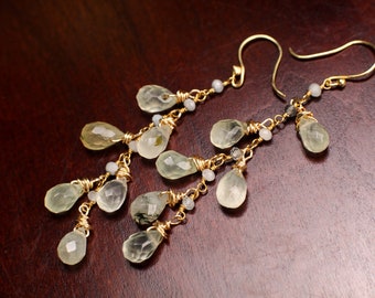 May include: A pair of gold dangle earrings with multiple teardrop-shaped green and white gemstones. The earrings are made with wire wrapped around each gemstone.