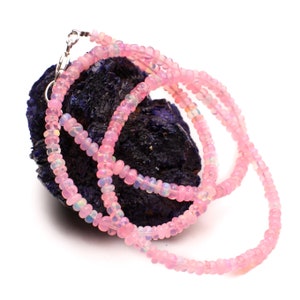 May include: A pink opal bead necklace with a silver clasp. The necklace is draped over a dark blue rock.