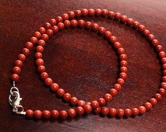 May include: A red gemstone bead necklace with a silver clasp. The necklace is made of round beads and is approximately 18 inches long.