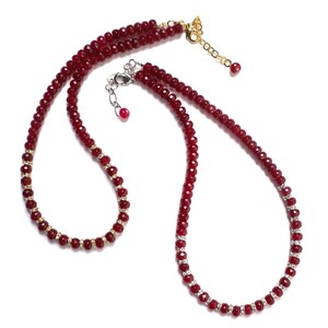 May include: A two-strand necklace with red beads and gold accents. One strand has clear rhinestones.