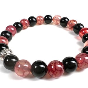 Puede incluir: Un brazalete hecho de cuentas de ágata negra y roja con un dije de plata. El brazalete está hecho de piedras naturales y es una excelente manera de agregar un toque de estilo a cualquier atuendo.