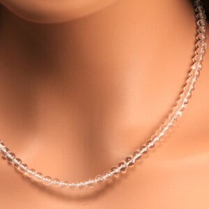 May include: A clear crystal beaded necklace on a model's neck. The necklace is made of small, round beads that are strung together on a thin cord.