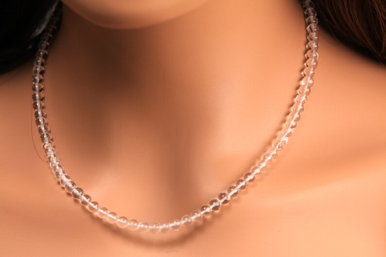 May include: A clear crystal beaded necklace on a model's neck. The necklace is made of small, round beads that are strung together on a thin cord.