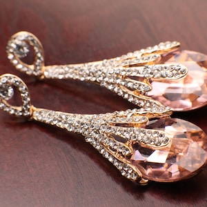 May include: A pair of gold tone dangle earrings with large pink teardrop shaped crystals and smaller clear crystals.