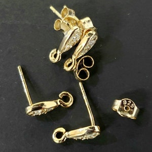 May include: Four gold-toned earring findings with clear crystal accents. The findings are marked "925" indicating they are made of sterling silver.