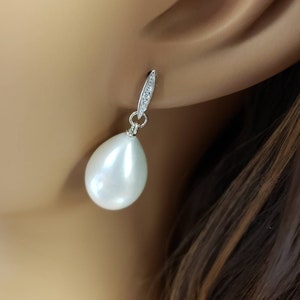 May include: A pair of silver dangle earrings with a white pearl drop and a small row of clear cubic zirconia stones on the top.