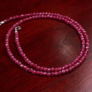 Puede incluir: Un collar de doble hebra compuesto por pequeñas piedras preciosas facetadas de color rojo intenso. El collar se asegura con un cierre plateado. Las piedras preciosas están dispuestas en una hebra continua, creando una joya delicada y elegante.