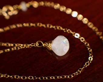 May include: A gold chain necklace with a white moonstone pendant. The moonstone is wrapped in gold wire.