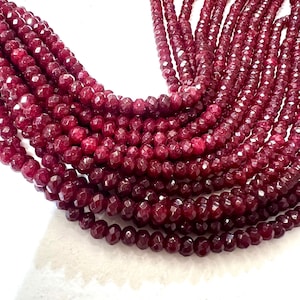 May include: A collection of multiple strands of deep red, faceted, round beads arranged in a curved formation. Each individual bead features a reflective, multi-faceted surface that catches the light, creating a uniform, dark crimson appearance.