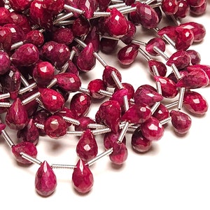 May include: A strand of faceted ruby gemstone beads in a teardrop shape. The beads are strung on silver wire.