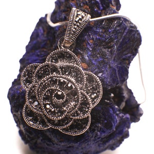 Könnte beinhalten: Ein silberner Anhänger in Form einer Blume mit schwarzen Edelsteinen. Der Anhänger befindet sich auf einem blauen Azurite-Stein.