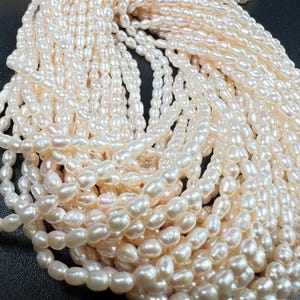 May include: A close-up view of multiple strands of creamy white freshwater pearls. The pearls have an irregular, oval shape and a lustrous sheen. The strands are arranged in a cascading pattern, creating a luxurious and elegant display.