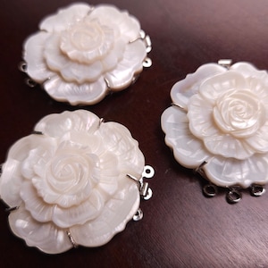Puede incluir: Tres abalorios de flor de madreperla blanca con lazos de metal plateado. Cada abalorio presenta un diseño de rosa tallada.