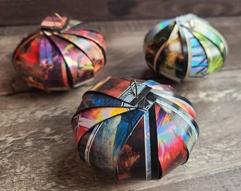 May include: Three spherical, origami-style paper ornaments. The ornaments have a multi-colored, iridescent finish with a variety of colors including red, blue, and green. The ornaments are arranged on a wooden surface.