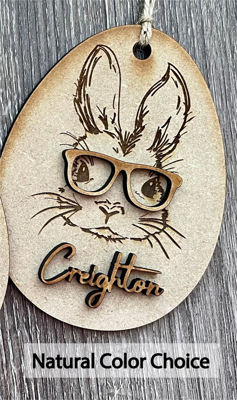 May include: Wooden Easter egg ornament with a laser-cut design of a bunny wearing glasses. The bunny's name, "Creighton", is written below the image. The ornament is a natural wood color.