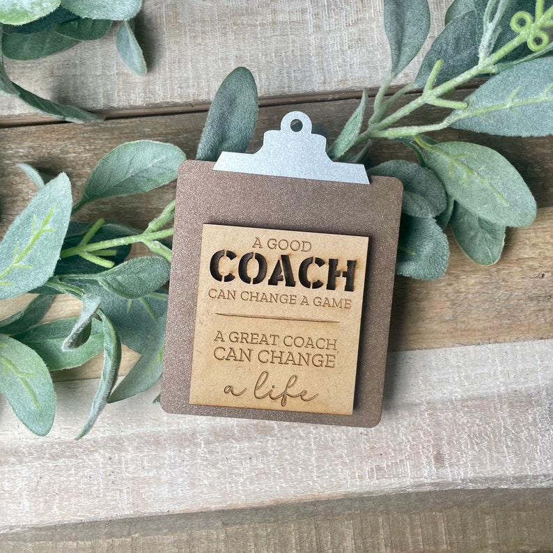 May include: A wooden sign with a clipboard design and the text "A good coach can change a game. A great coach can change a life."