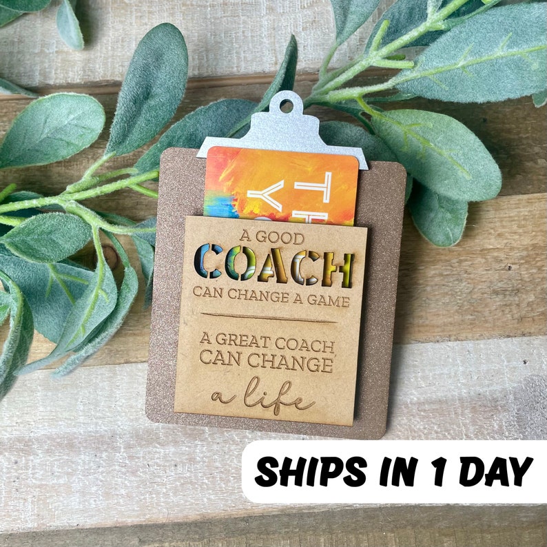 May include: A wooden gift card holder with a cutout design that reads "A good coach can change a game. A great coach can change a life." The holder has a slot for a gift card and a silver metal clip.