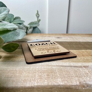 May include: A wooden sign with the text "A good coach can change a game. A great coach can change a life."