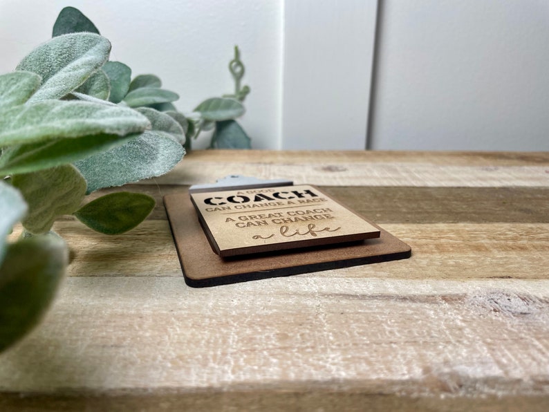 May include: A wooden sign with the text "A good coach can change a game. A great coach can change a life."