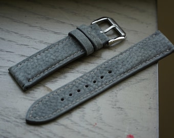 May include: A gray leather watch strap with a silver buckle. The strap has a textured surface and is stitched with white thread.