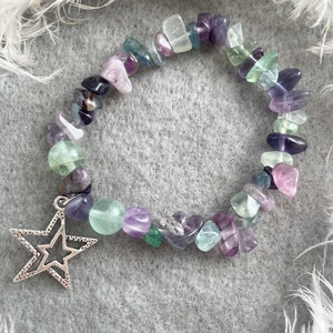 May include: A multi-colored gemstone bracelet with a silver star charm. The bracelet features various shades of purple, green, and blue gemstones.