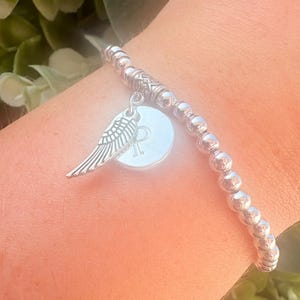 Pulsera plateada con inicial de ala de ángel: joyería personalizada para el duelo