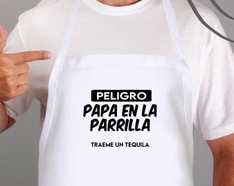 May include: White apron with black text that reads "PELIGRO PAPA EN LA PARRILLA TRAEME UN TEQUILA" and the social media handle "@bululu.atl".