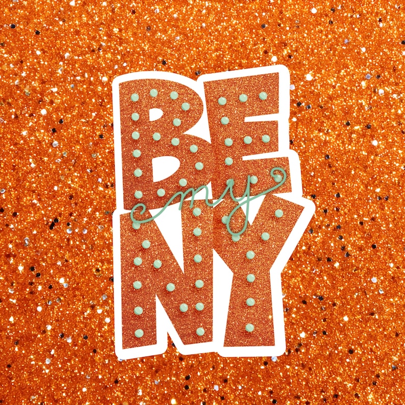 May include: A sticker with the words "BE my NY" in orange glitter letters with light blue polka dots. The words are outlined in white, and the background is orange glitter.