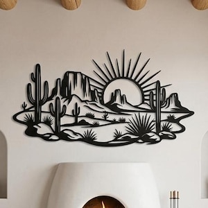 A black laser-cut metal desert sunset art piece hangs on a white wall above a fireplace in a living room.