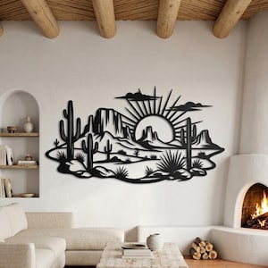 Può includere: Un'opera d'arte da parete in metallo nero che raffigura la silhouette di un paesaggio desertico. Il design include cactus saguaro, formazioni rocciose e un sole nascente con raggi e nuvole. L'opera è montata su una parete bianca.