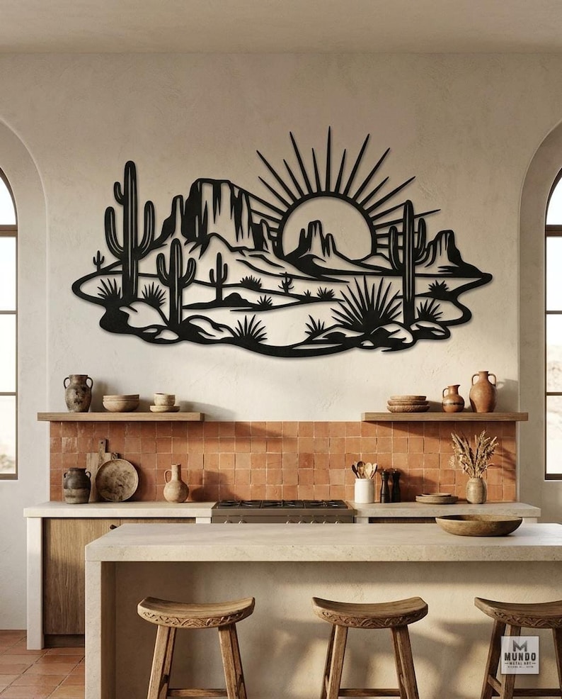 A black metal desert landscape wall sculpture is displayed on a tiled kitchen wall above a counter.