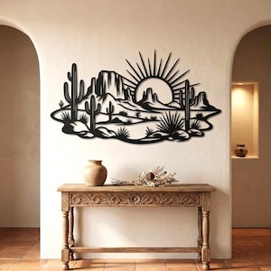 A black saguaro cactus and desert sunset metal wall sign is mounted above a carved wooden console table.