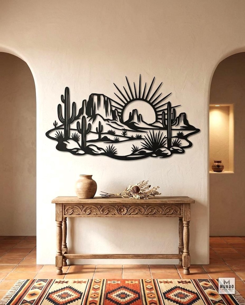 A black saguaro cactus and desert sunset metal wall sign is mounted above a carved wooden console table.