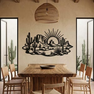 A black metal desert art piece hangs on a dining room wall above a large wooden table.