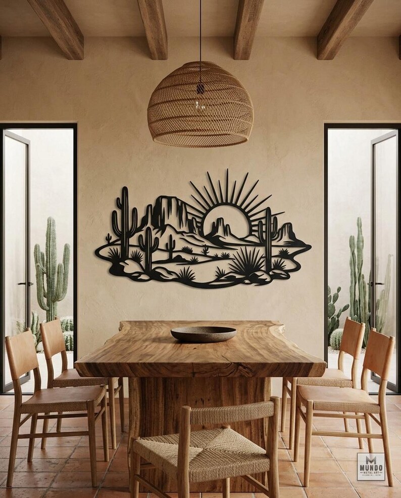 A black metal desert art piece hangs on a dining room wall above a large wooden table.