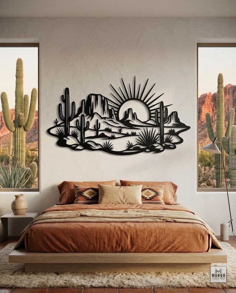 A black metal desert sunset sign is centered on a bedroom wall above a platform bed with orange bedding.