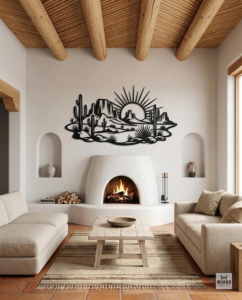 A black laser-cut metal desert sunset art piece hangs on a white wall above a fireplace in a living room.
