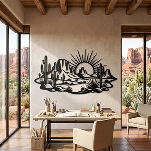 A black metal desert sunset wall hanging is mounted in a bright studio workspace overlooking red rock formations.