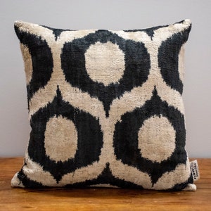 May include: Black and white geometric patterned cushion with a subtle sheen. The cushion is made of velvet and has a fringed edge.