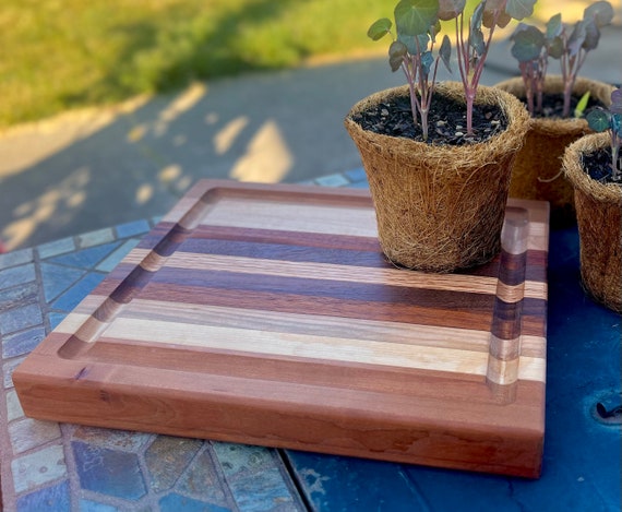 Edge-grain cutting board in a trio of premium hardwoods — custom personalization elevates it from tool to heirloom.
