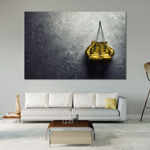 May include: A pair of gold boxing gloves hanging on a hook against a textured gray wall.